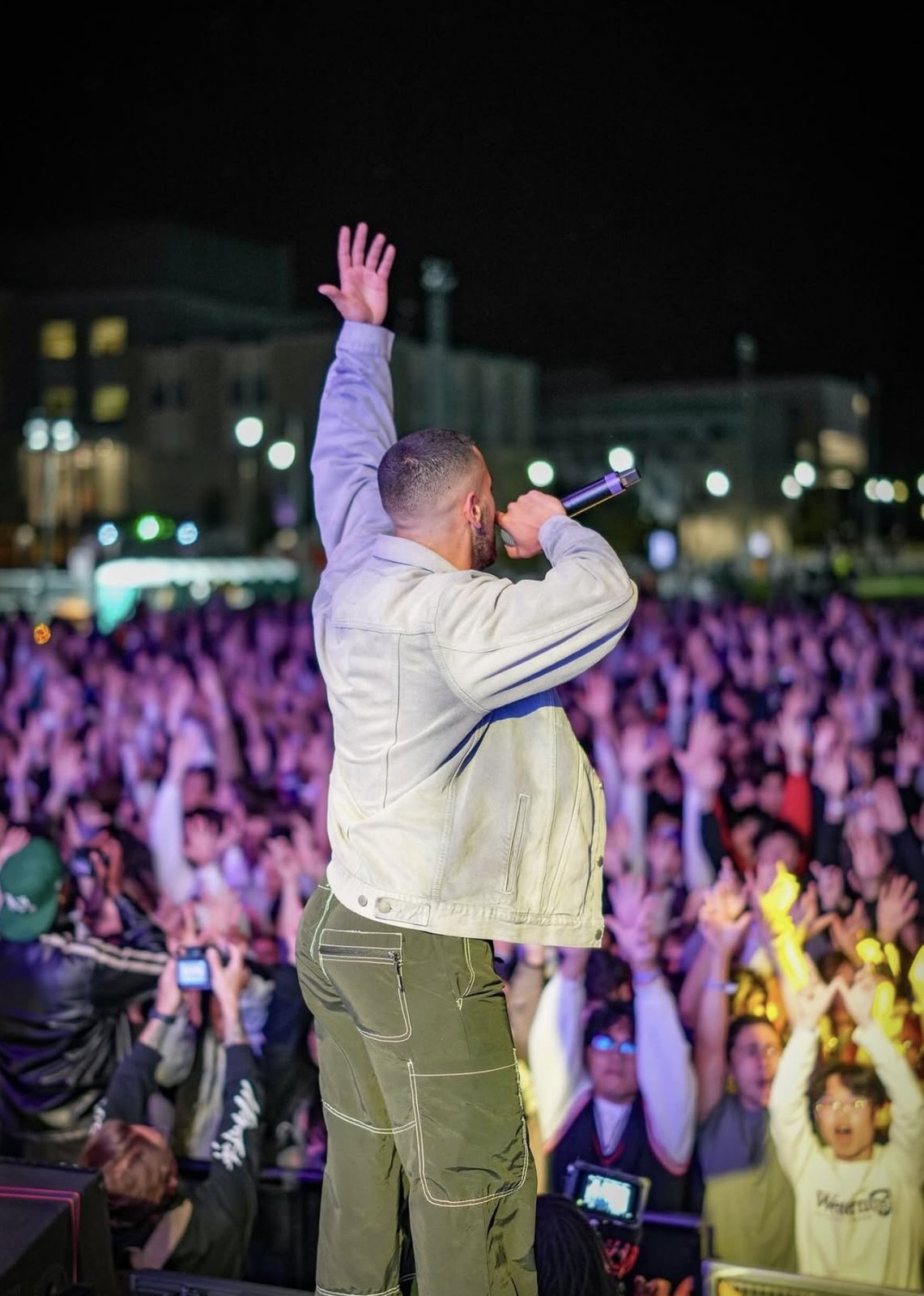 Performer waving toward a packed outdoor audience from the stage