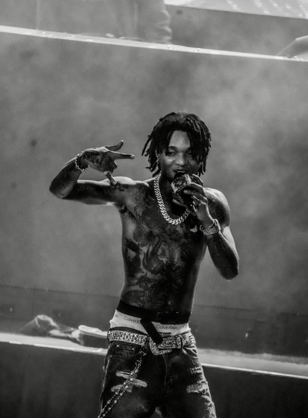 Shirtless performer moving across a smoke-filled stage