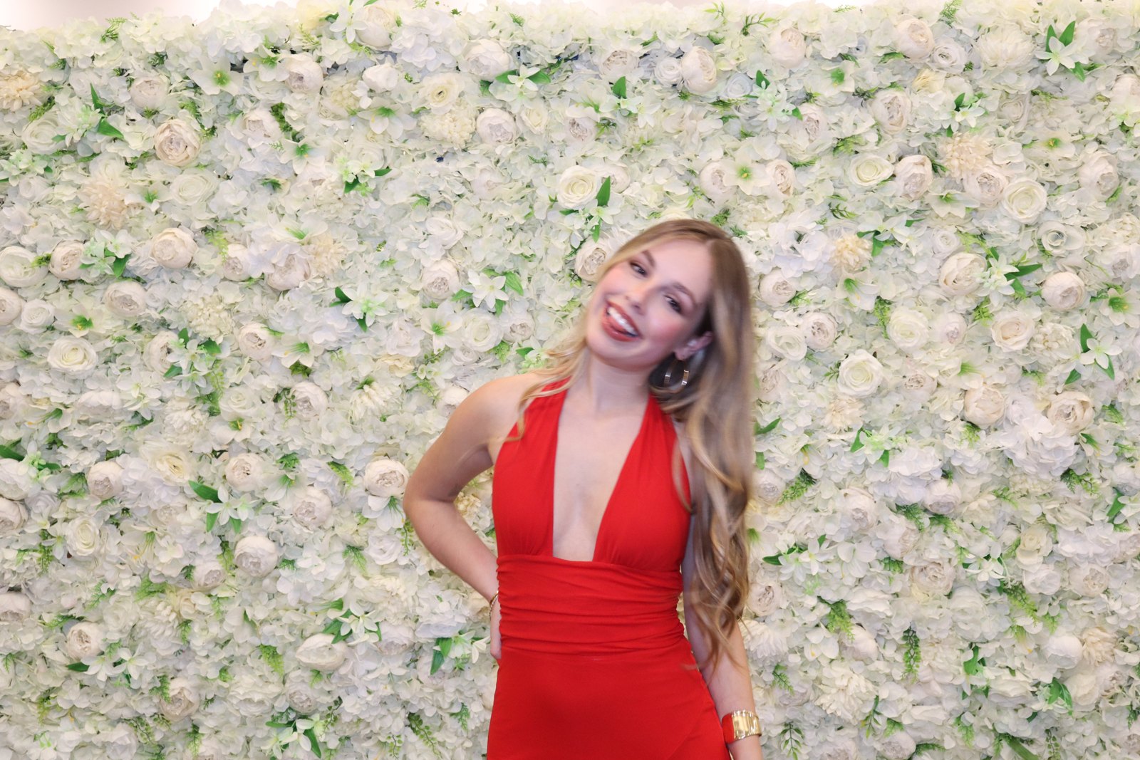 Guest in a red dress posing in front of a cream flower wall