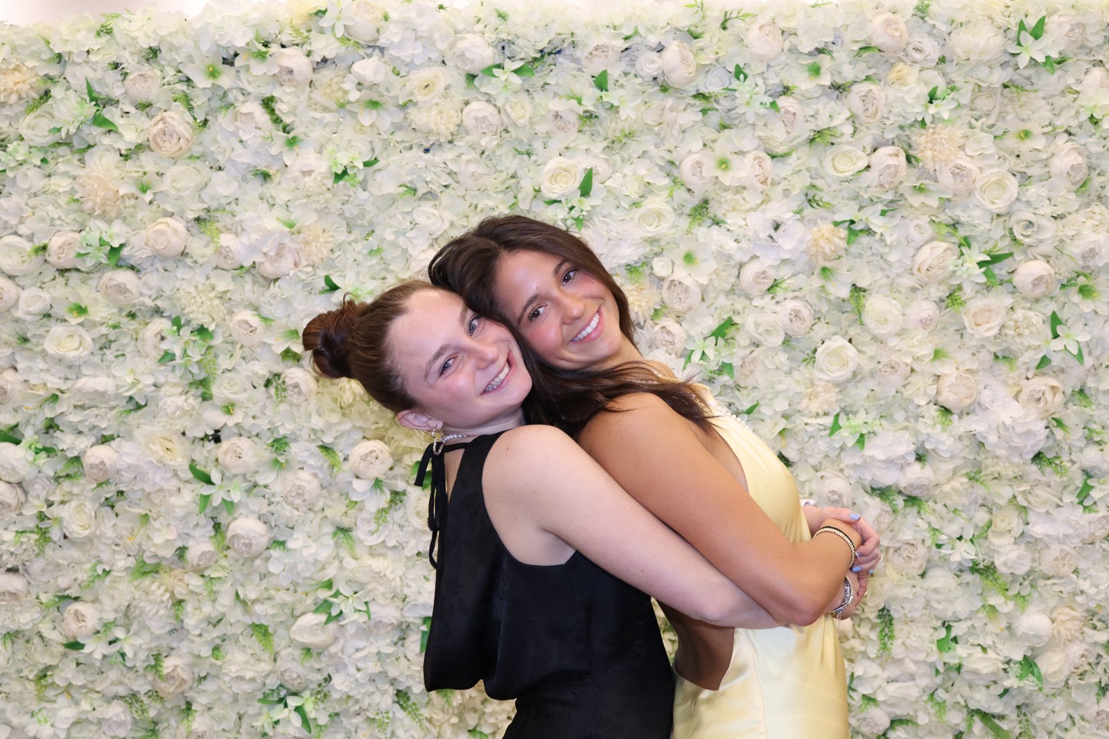 Two guests embracing in front of a cream flower wall